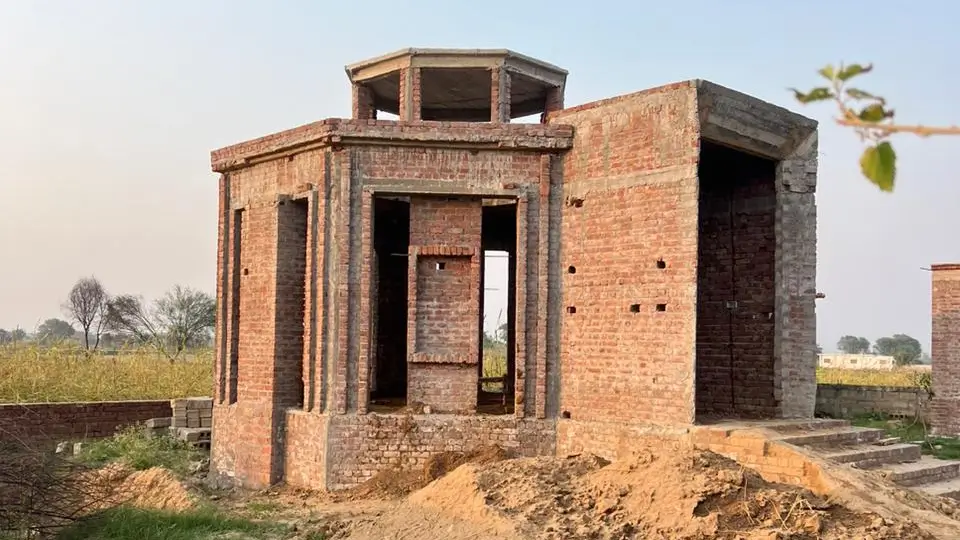 small mosque under construction with fields behind it and stairs also under construction