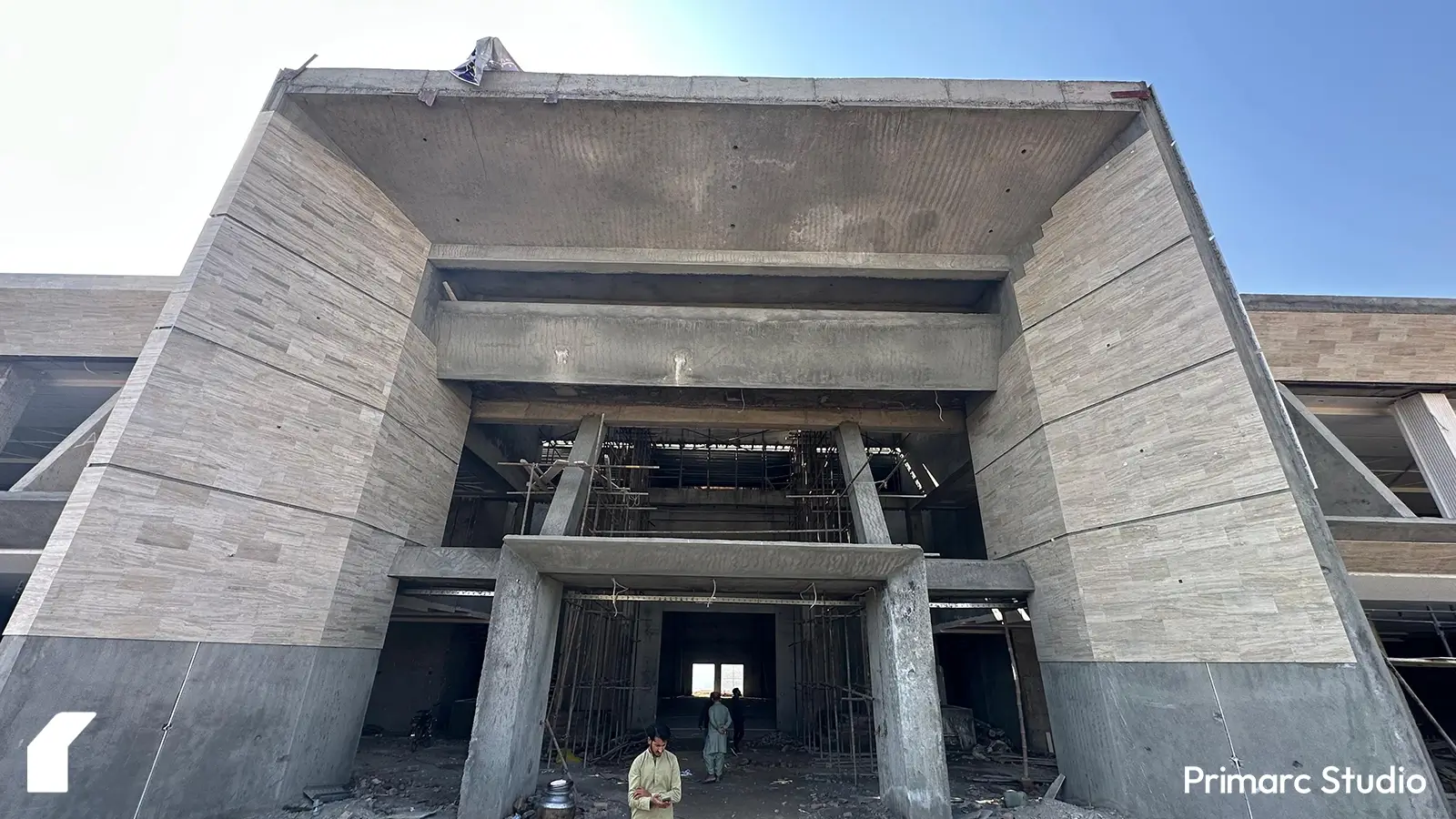 Close-up of the triple-height entry portal of a modern marquee in Islamabad, with laborers carefully installing travertine cladding on the facade. The intricate craftsmanship highlights the premium materials used in the contemporary architectural design.