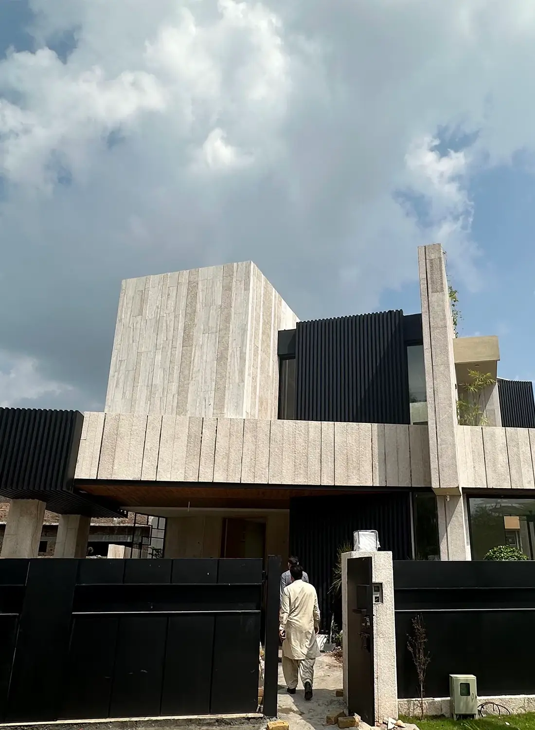 View of a unique modern architectural style house exterior in Islamabad, featuring travertine and black vertical elements, showcasing the distinctive design of this contemporary 1 kanal residence for sale in Gulberg Greens.