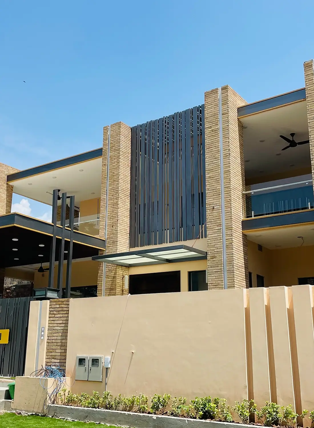 Exterior view of a modern 1 Kanal residential facade in F-11, Islamabad, designed by Primarc Studio. The contemporary architectural design prominently features small brick (Gutka) cladding, striking vertical elements suggesting columns, and modern metal strip detailing. This image highlights the distinctive facade of the Primarc Studio project.