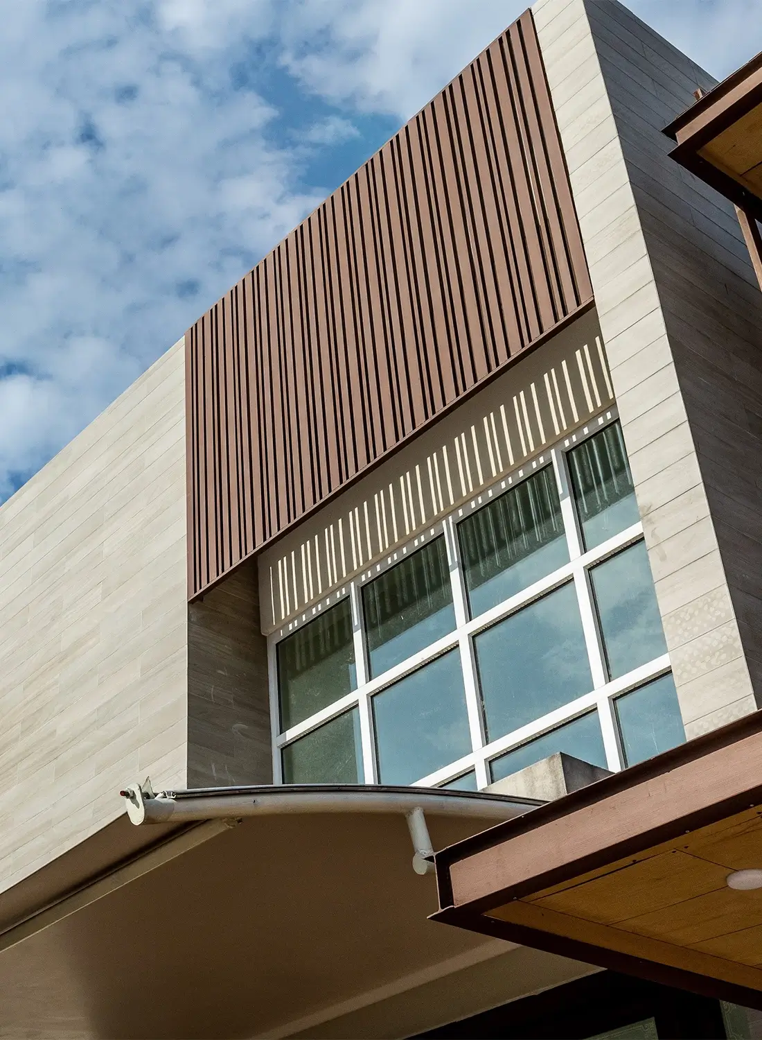 Close-up view of the modern facade of a 1 Kanal house in Bahria Enclave Islamabad, showcasing clean lines, the blend of brown powder-coated metal and cream-coloured stone cladding, and contributing to the minimalist exterior design of this contemporary residence.
