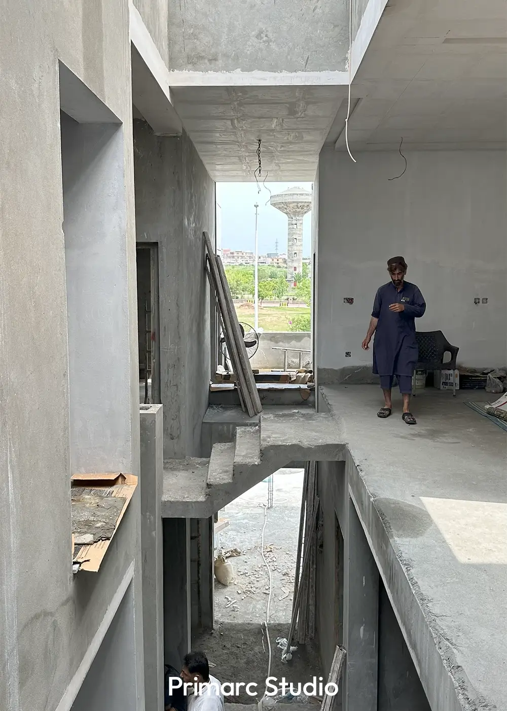 Multi-level interior space of a minimalist house under construction, featuring an open stairwell and a view of the surrounding neighborhood.