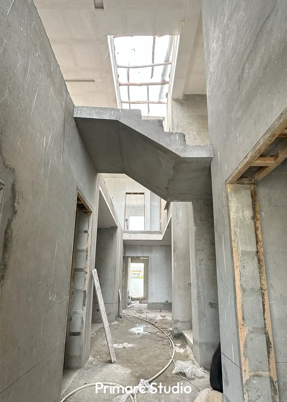 Interior view of a minimalist house under construction, showing a concrete staircase and open spaces leading to a skylight.