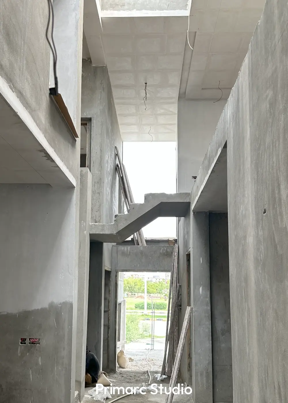 Interior hall of a minimalist house under construction, featuring a floating concrete staircase and view to the outside.