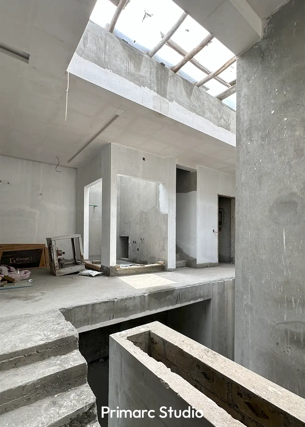 Interior of a minimalist house under construction, showcasing a multi-level space with a large skylight structure.