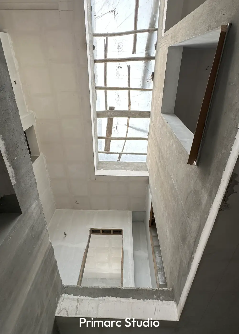 Upward view inside a minimalist house under construction, focusing on a large skylight and concrete ceiling details.