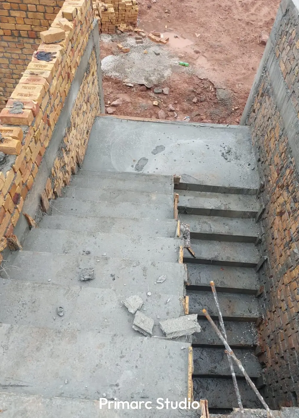 Top-down view of a newly cast concrete staircase descending into a lower level, flanked by brick walls.