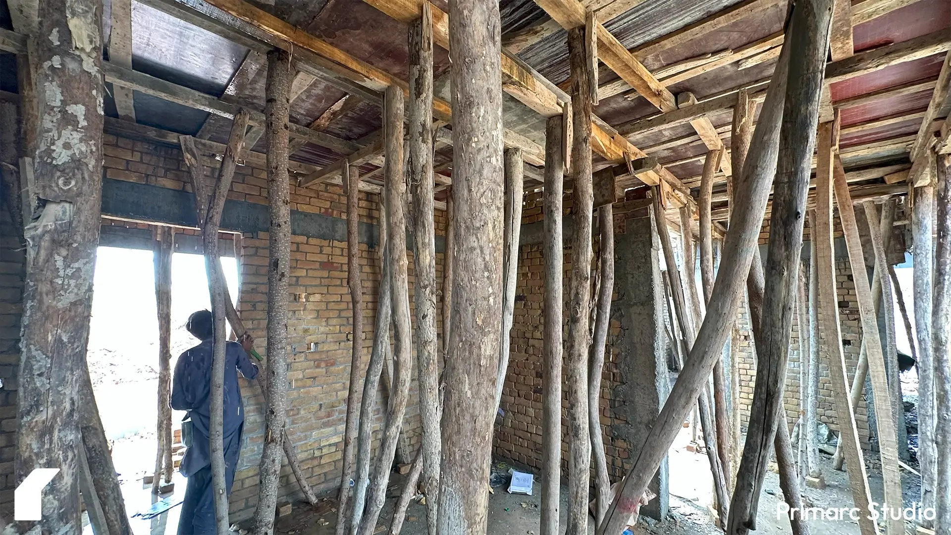 Interior view of a house under construction with brick walls and extensive wooden scaffolding supporting the ceiling formwork.