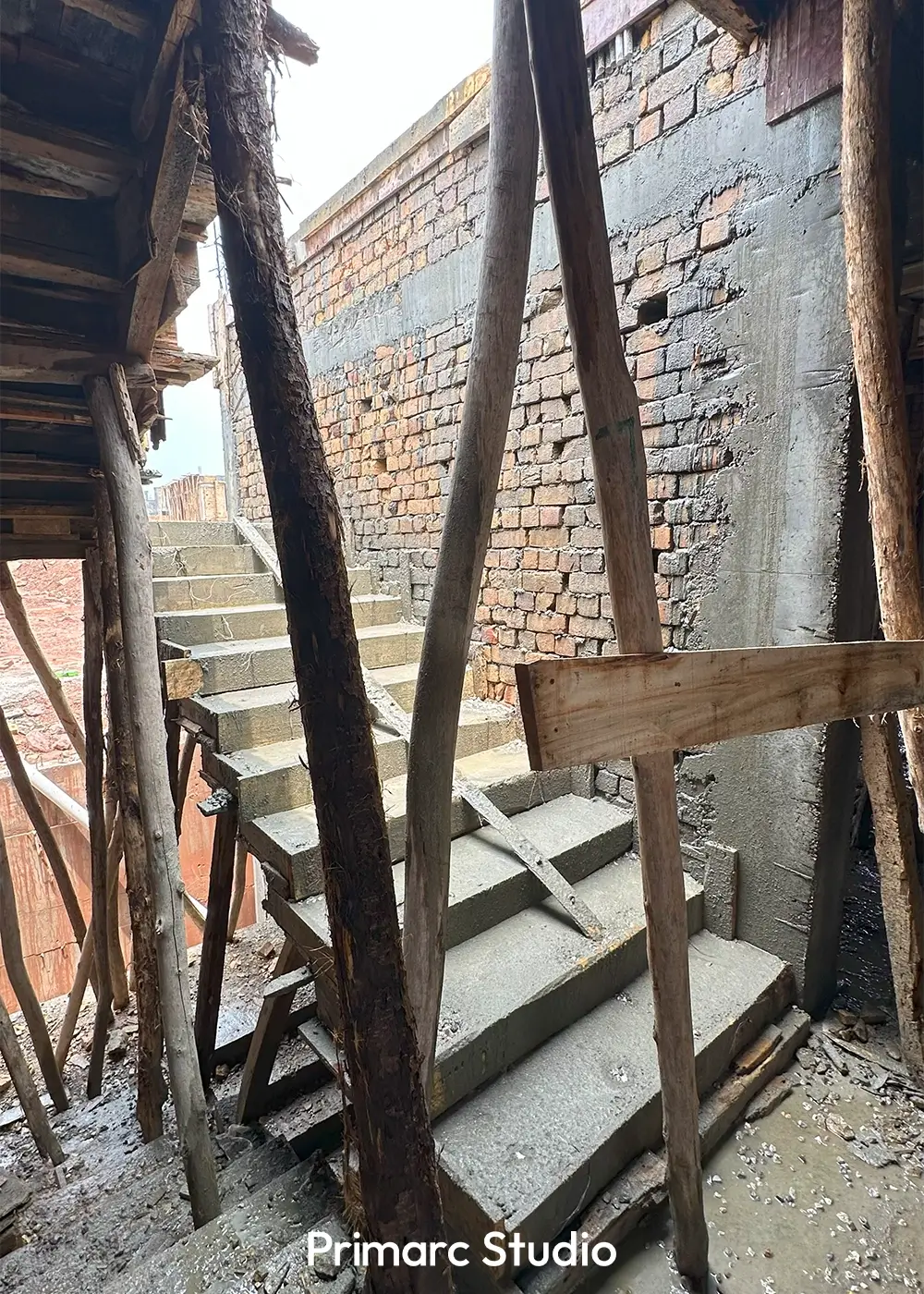 Concrete staircase under construction, surrounded by wooden scaffolding and newly laid brick walls.