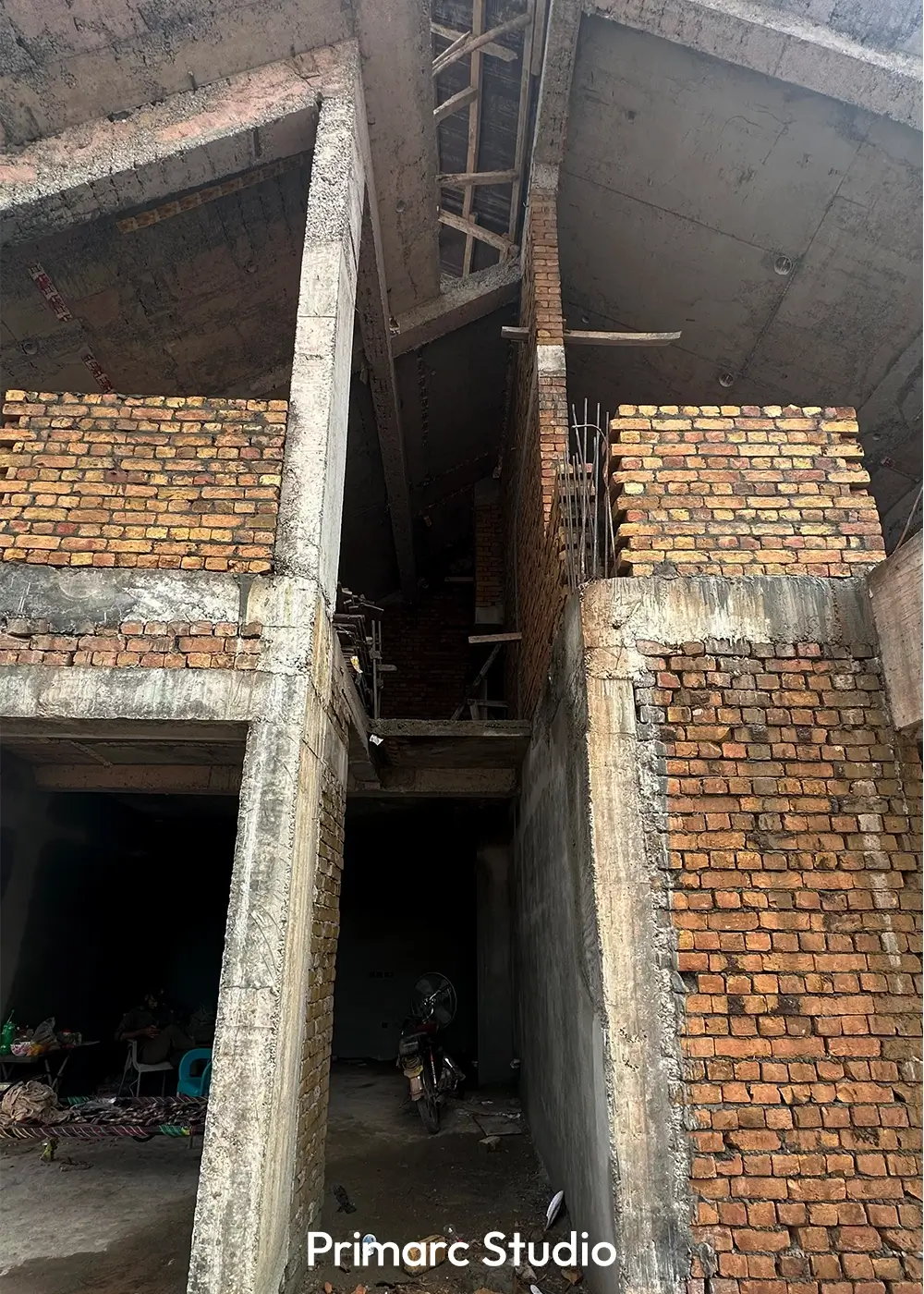 Close-up view of under-construction double-height entry space with exposed brick walls and unfinished concrete beams in a contemporary Islamabad residence.