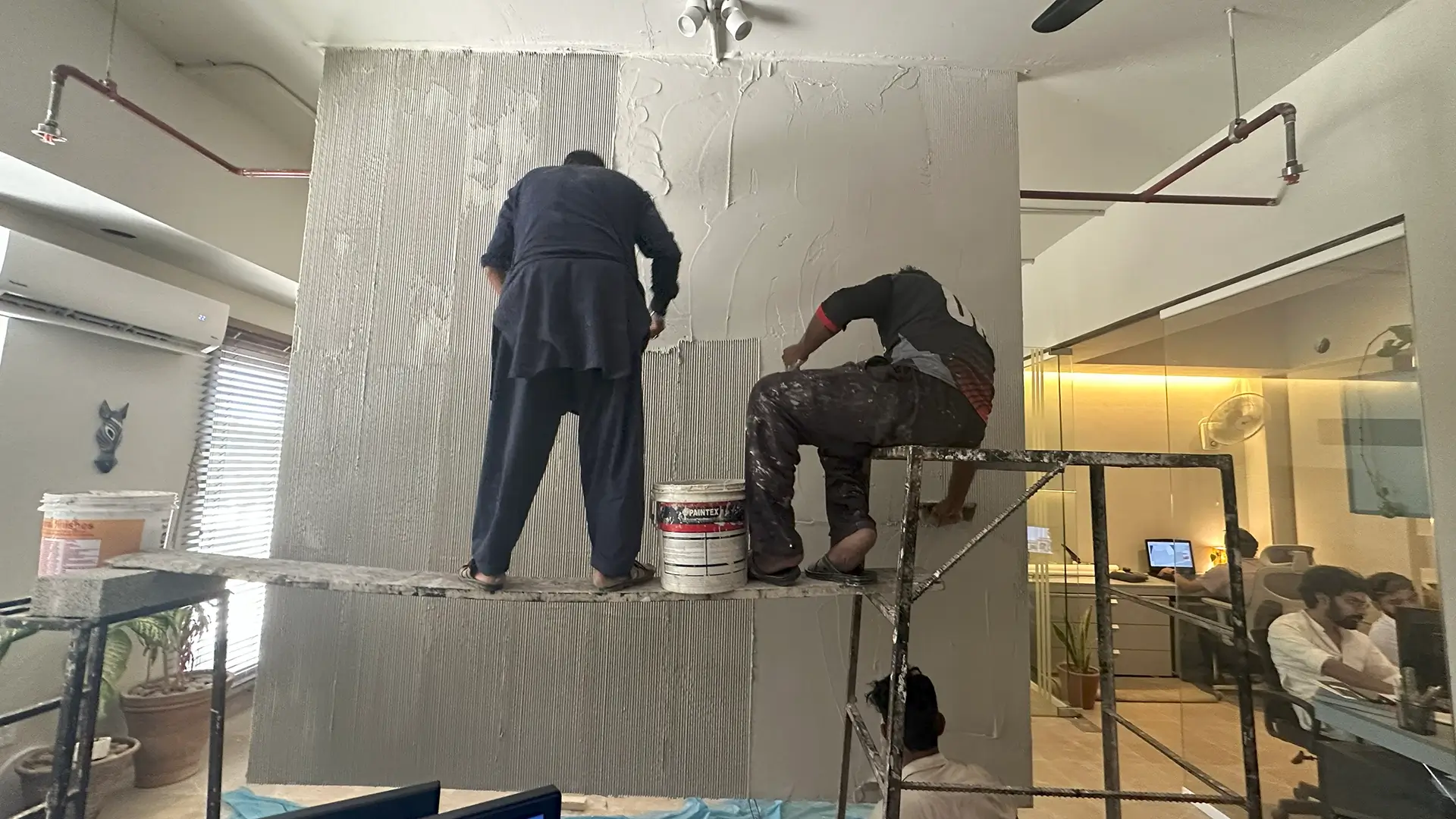 Workers applying textured plaster finish on interior wall during Primarc Studio office renovation in Islamabad
